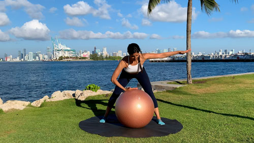 Starting position for spine rotation stretch with a stability ball, feet wide and hand on ball