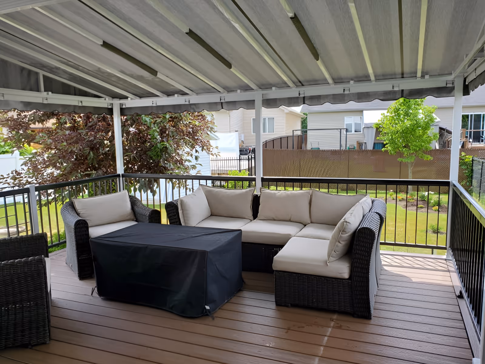 Covered backyard deck with patio furniture arrangement on brown wooden decking.