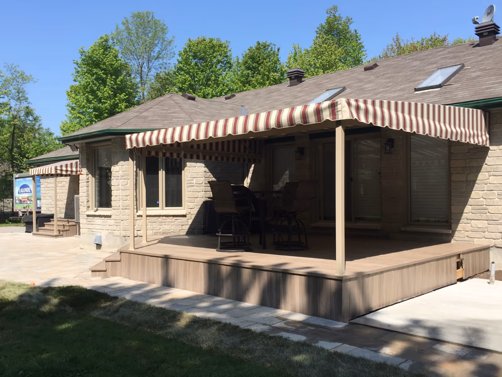 Patio and entrance with striped fixed awnings attached to a stone house with outdoor seating under the awning on a sunny day.