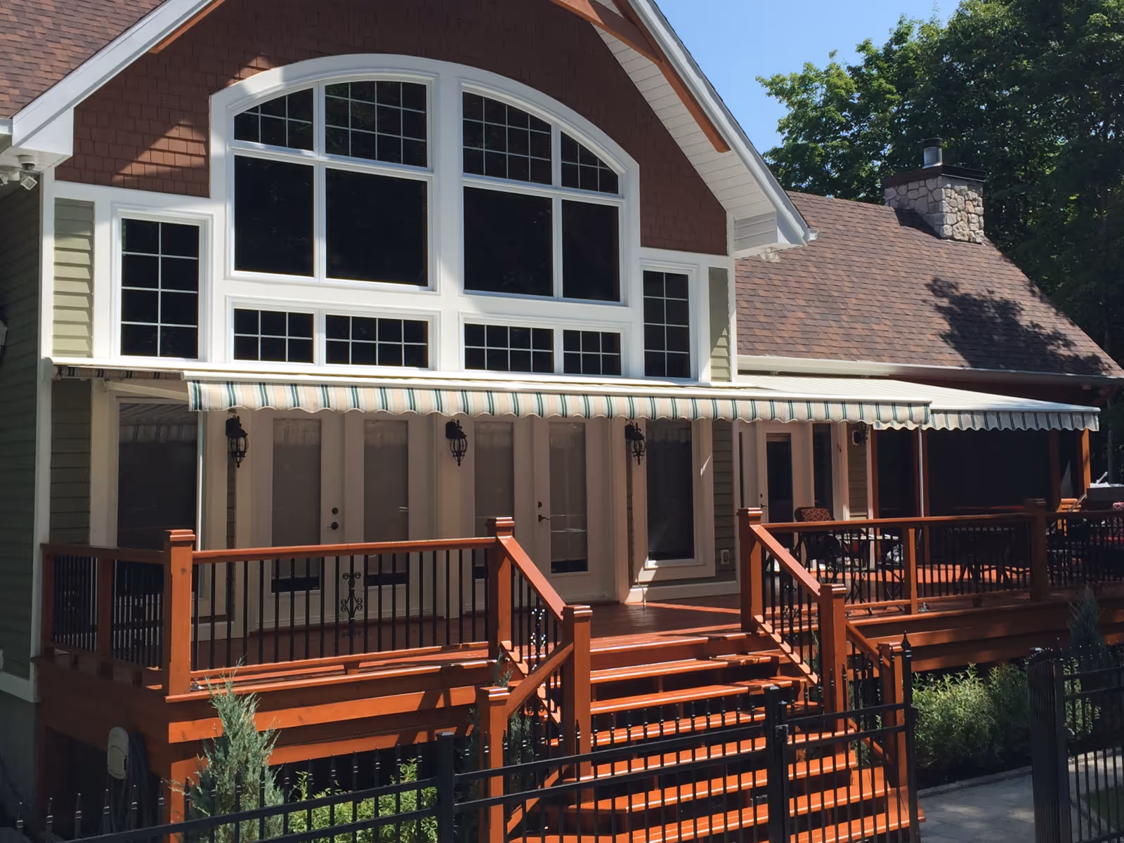 House with large arched windows, a  a wooden deck, and a striped retractable awning halfway extended.
