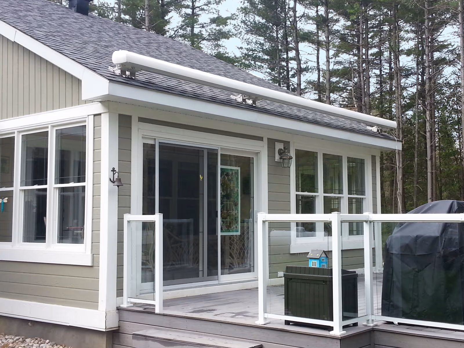 Roof-mounted retractable awning installed above sliding glass doors on a house with a glass-railed deck.