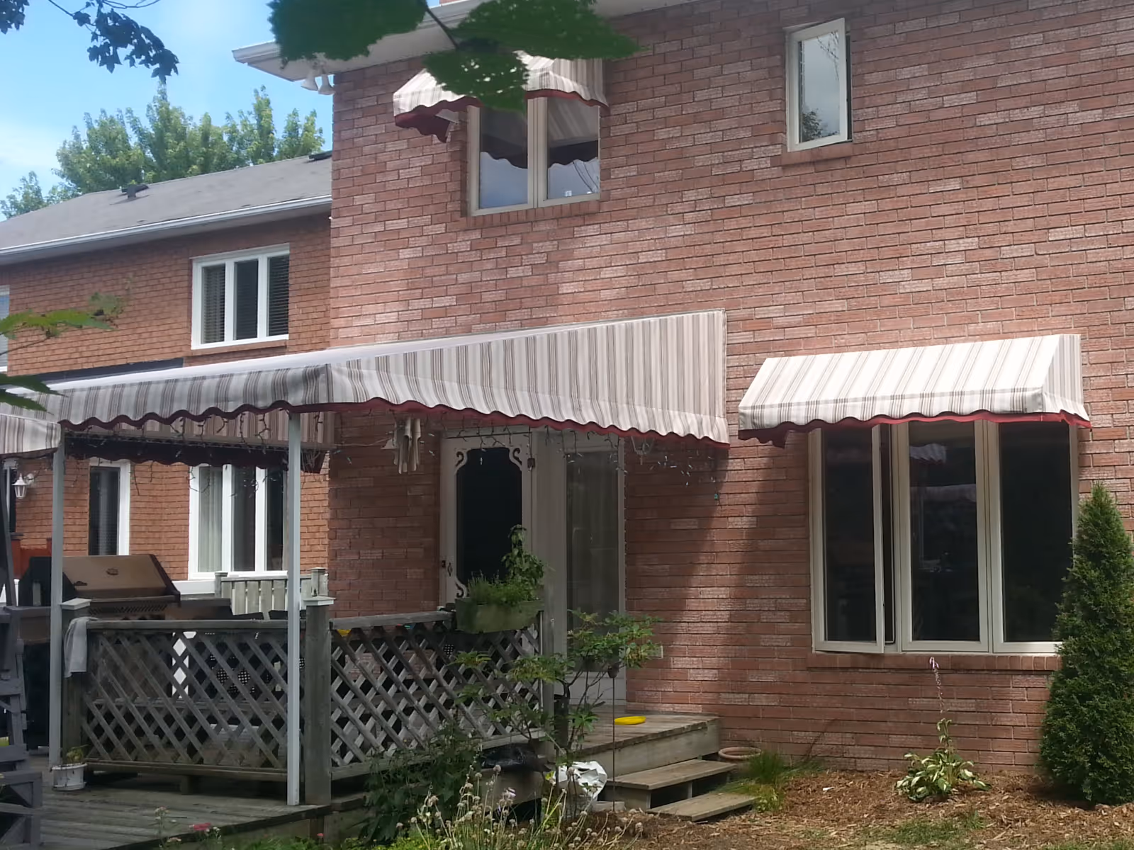 Brick house exterior with beige and white striped fabric awnings over windows and a patio door.