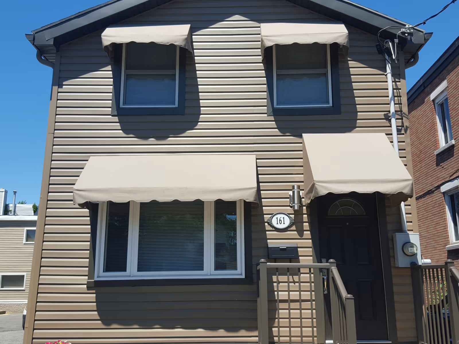 Front of beige two-storey house with four light beige-colored awnings over windows and door.