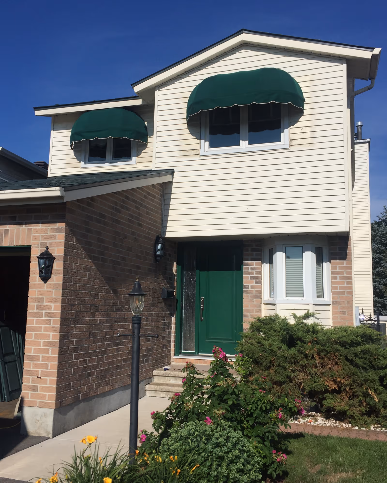 House exterior with dark green-painted front door with matching green bullnose awnings over two second-storey windows.