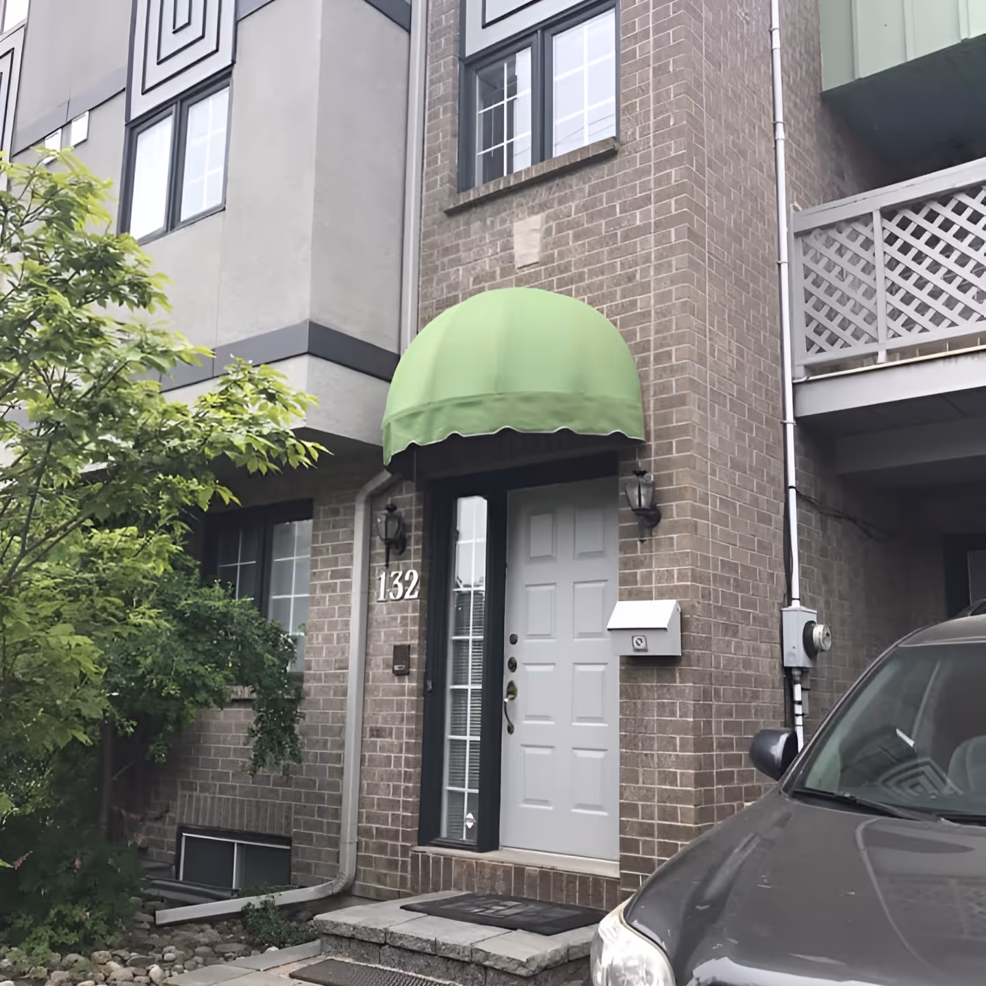 Front entrance of a brick townhouse with white door and a dome awning with a green fabric cover.