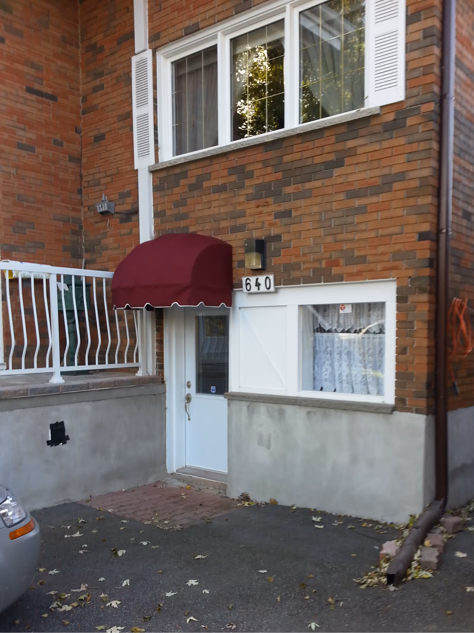 White door with burgundy clamshell awning on brick and concrete building exterior.