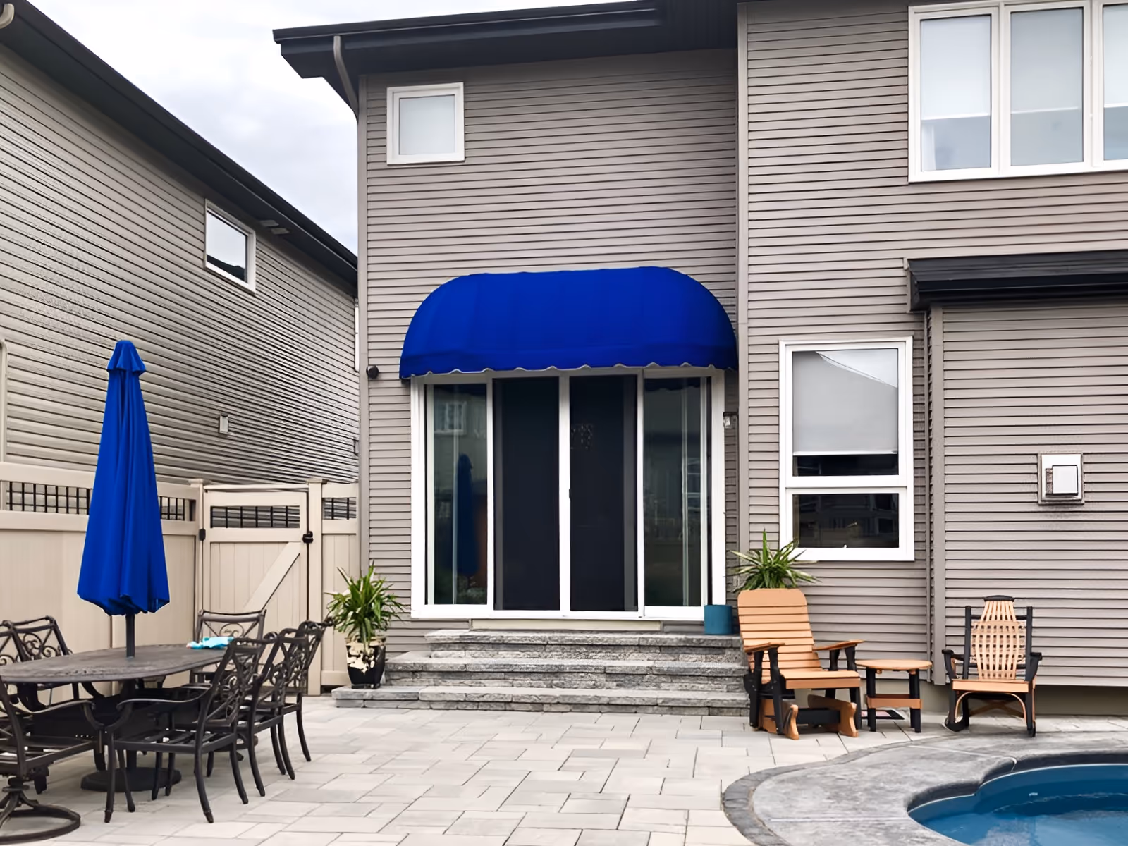 Bullnose awning over backyard patio door of two storey house with blue fabric that matches the blue patio umbrella.