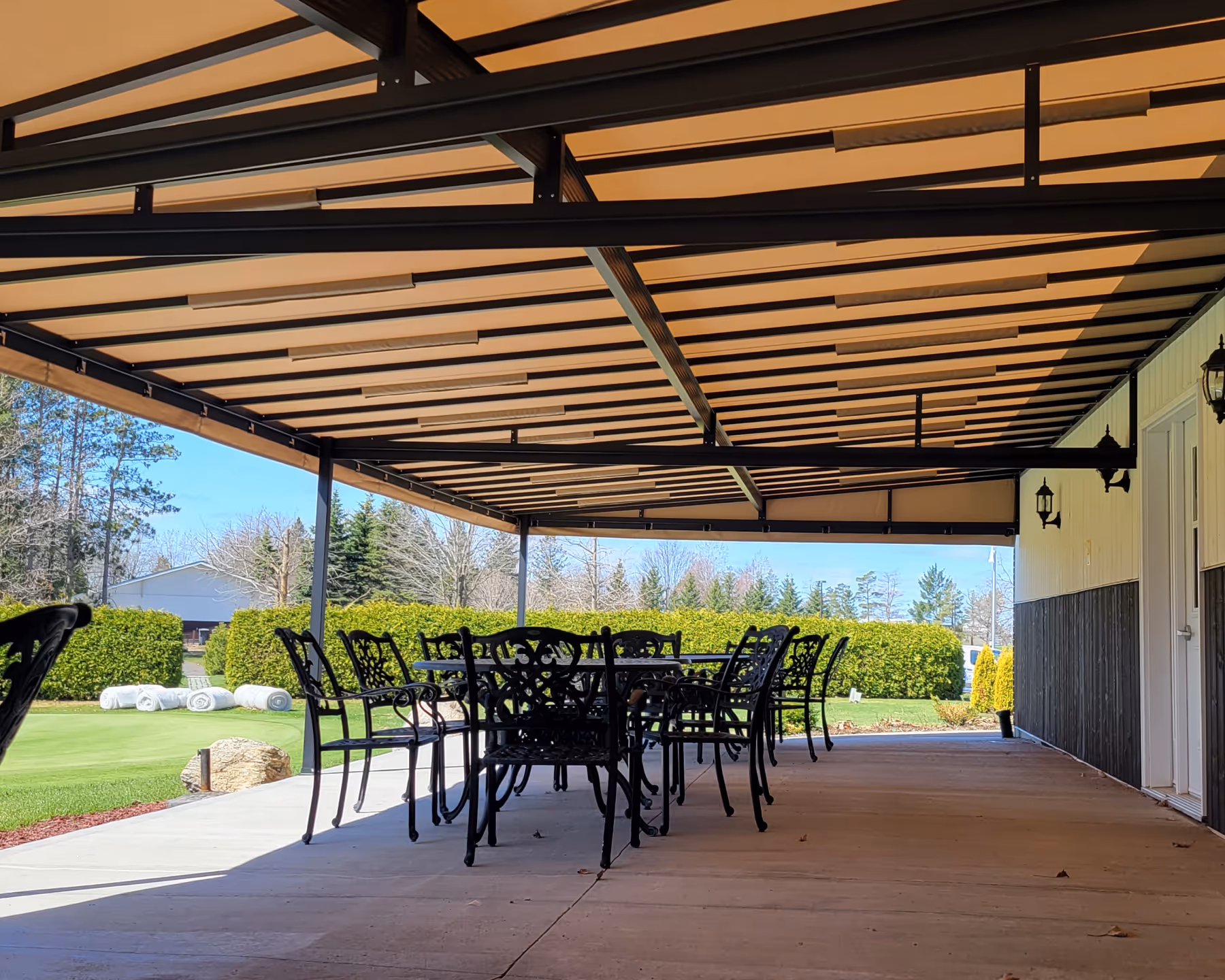 A large stone patio with tables and chairs at a golf course restaurant shaded by a fixed awning.