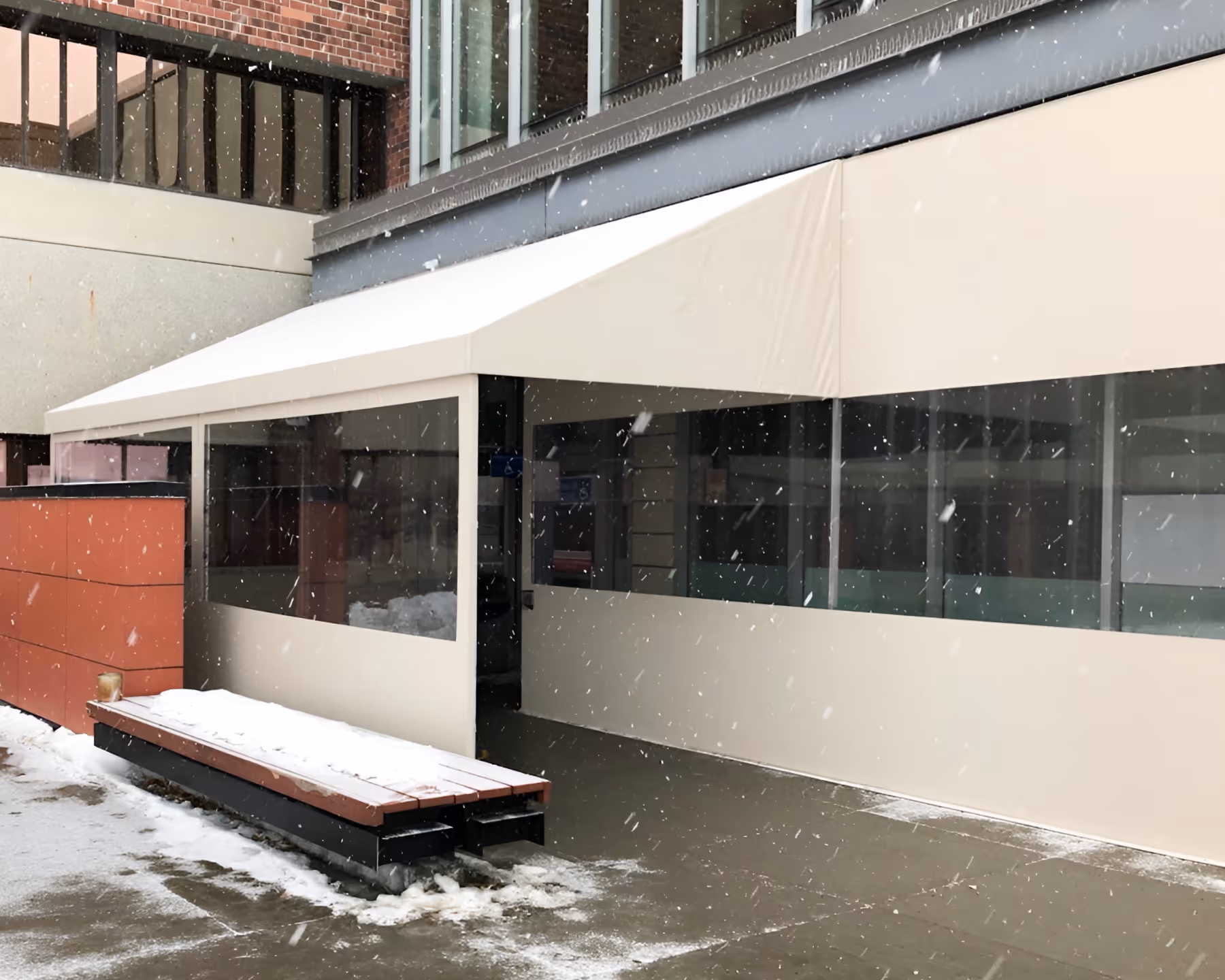 An awning and fabric panels with clear plastic windows cover a hospital entrance on a snowy day.