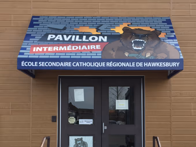 Entrance of a school with a blue awning showing a roaring bear and the school's name.