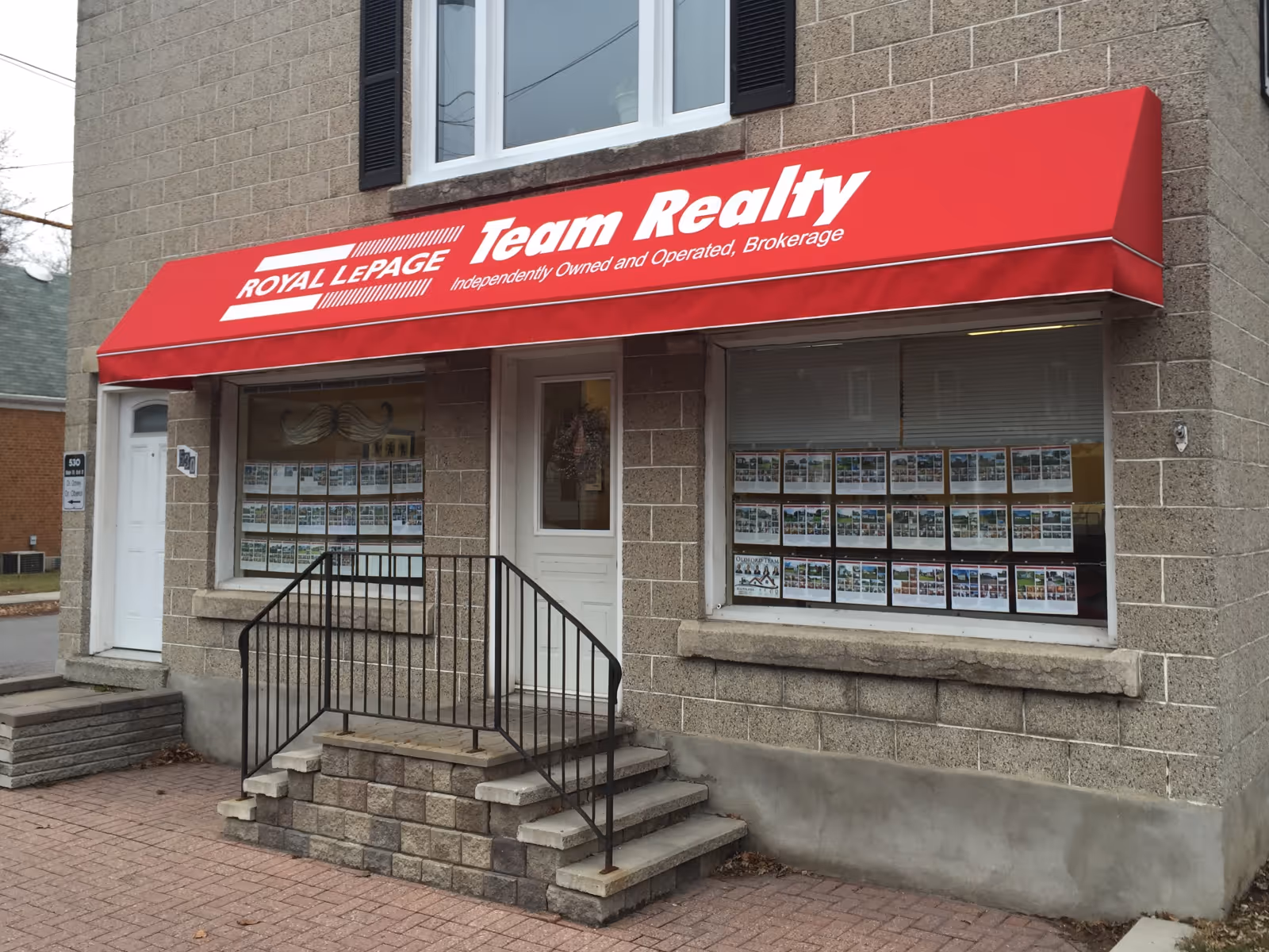 Red awning with Royal LePage Team Realty branding above office entrance in grey stone building.
