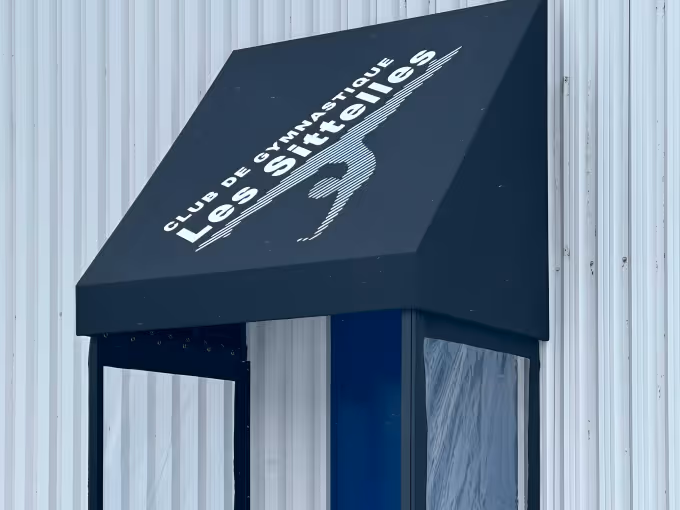 Black entrance awning with 'Club de Gymnastique Les Sittelles' text and logo over a blue door set in a white corrugated metal wall.