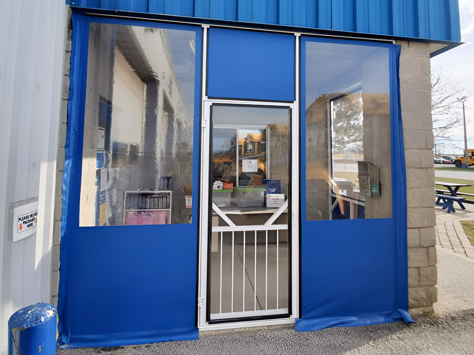 Entrance with a white metal door framed by blue vinyl fabric panels with large clear vinyl windows.