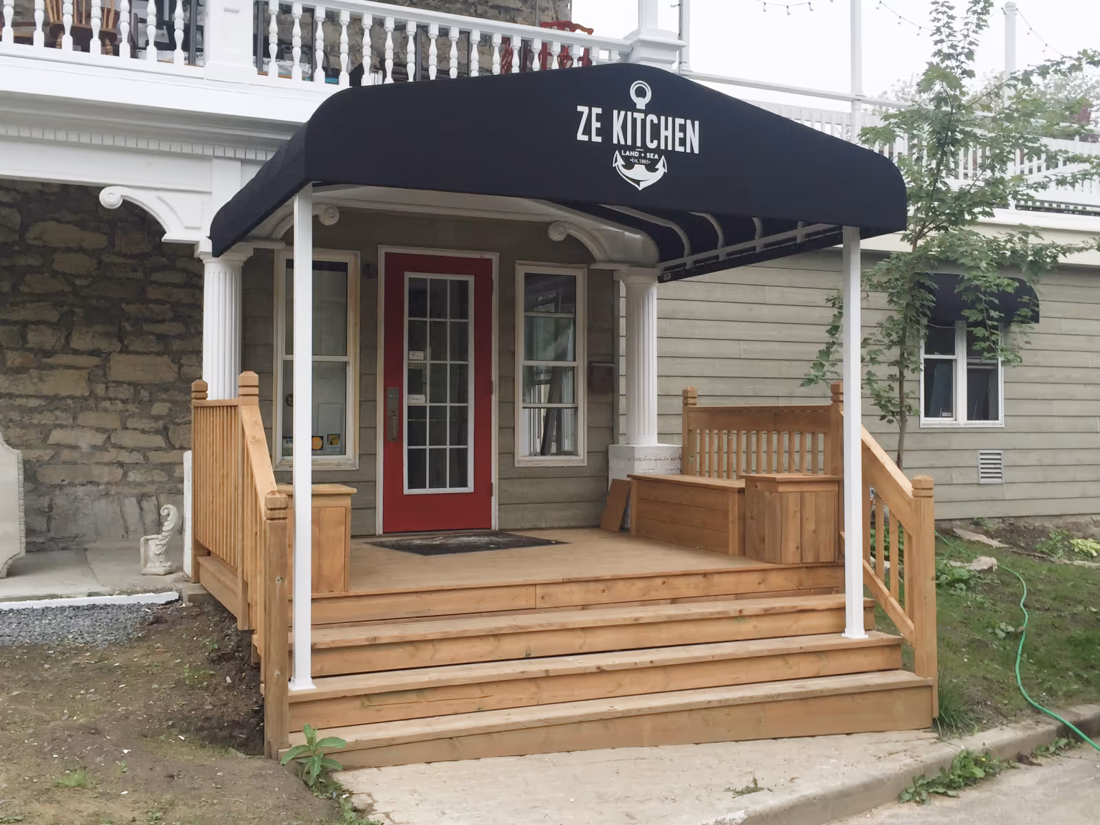 Front entrance of a restaurant with a red door, wooden steps and a black awning.