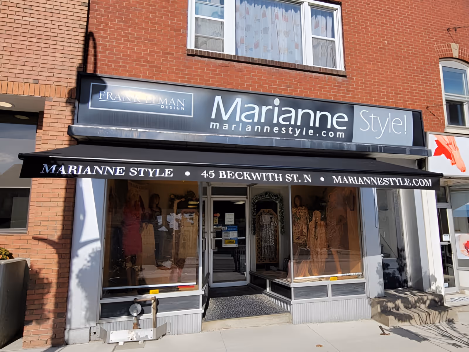 Storefront of Marianne Style boutique with black retractable awning displaying the street and website addresses.