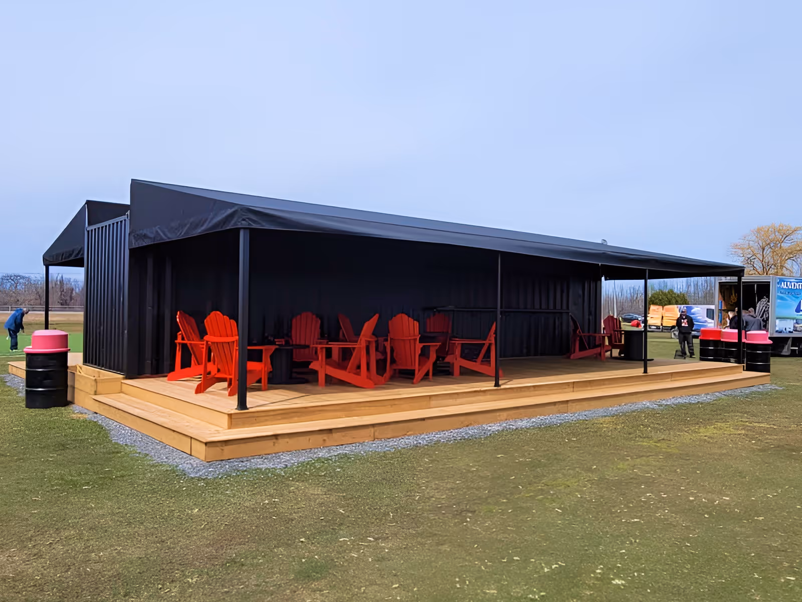Outdoor seating area of driving range made of a repurposed shipping container with black awnings on both long sides.