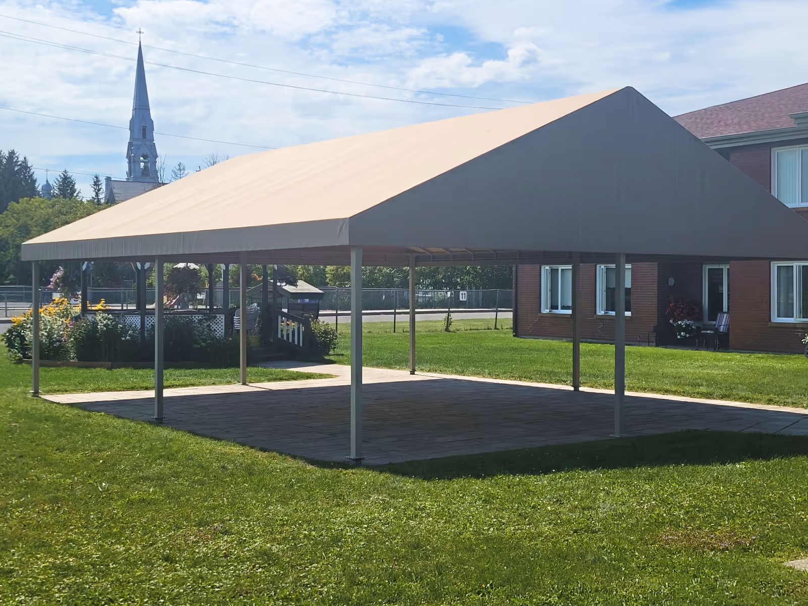 Large A-frame gazebo over a stone patio in the middle of a grassy lawn.