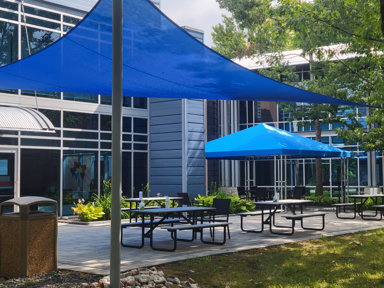 Outdoor courtyard with blue shade sail and gazebo with blue cover over separate seating areas.