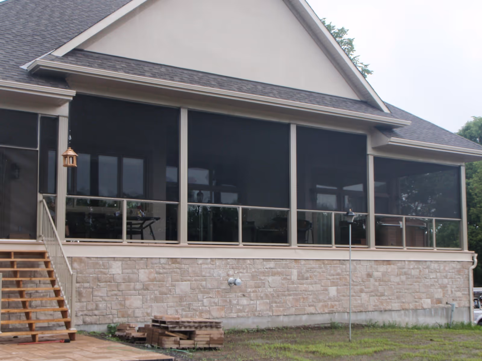 Tension screens with tan aluminum frames and glass railings create a screened-in porch spanning the width of a large house.