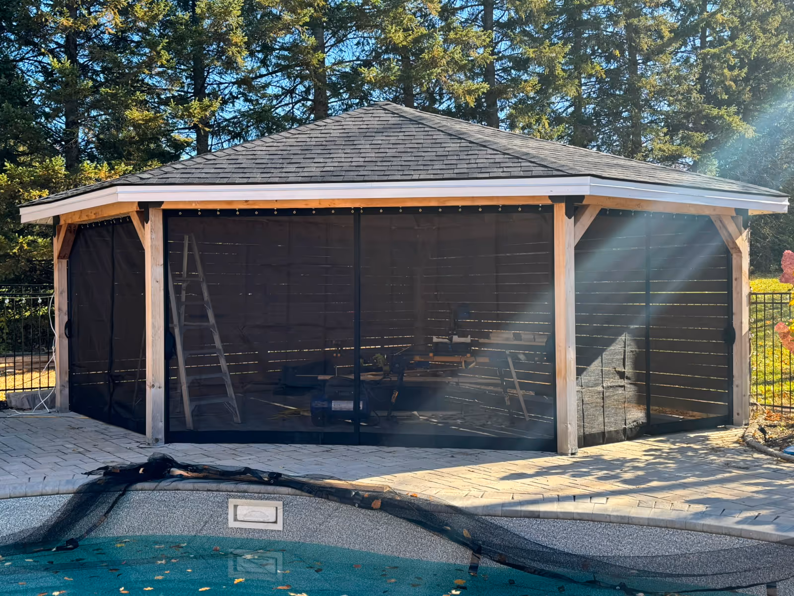 A hexagonal wooden gazebo slatted walls on three sides and curtain screens on the remaining three.