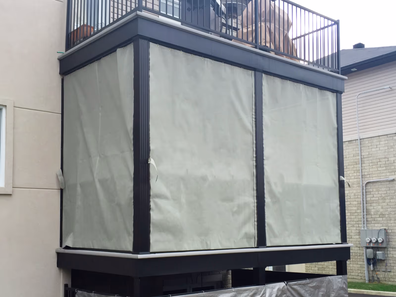 Grey sun mesh curtains enclose the space beneath a second-storey deck.