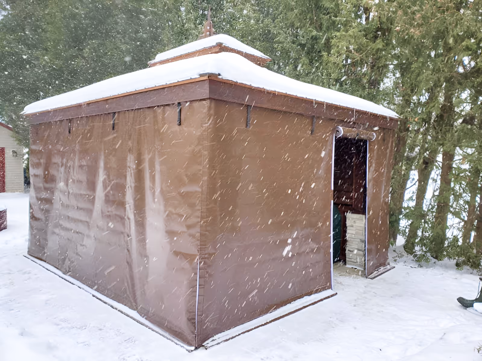 Snow falls around a square gazebo, whose sides are covered by brown vinyl panels.