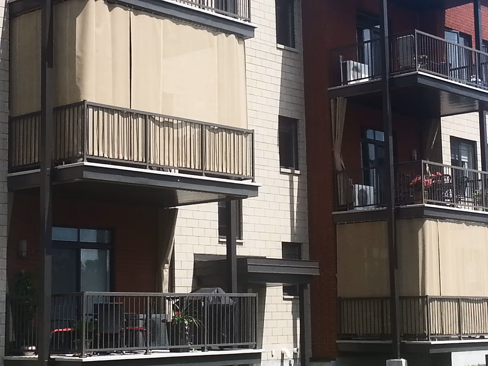 Balconies on a high-rise building with tall beige sun mesh curtains.