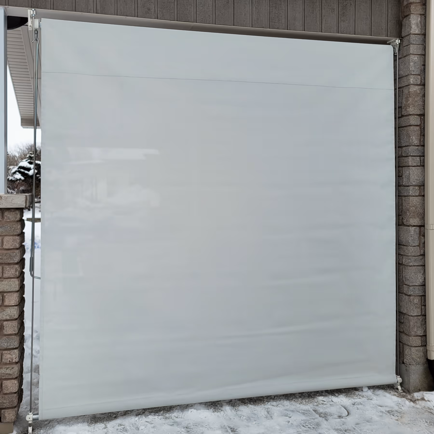 An exterior roller blind with grey sun mesh conceals the space next to a house.