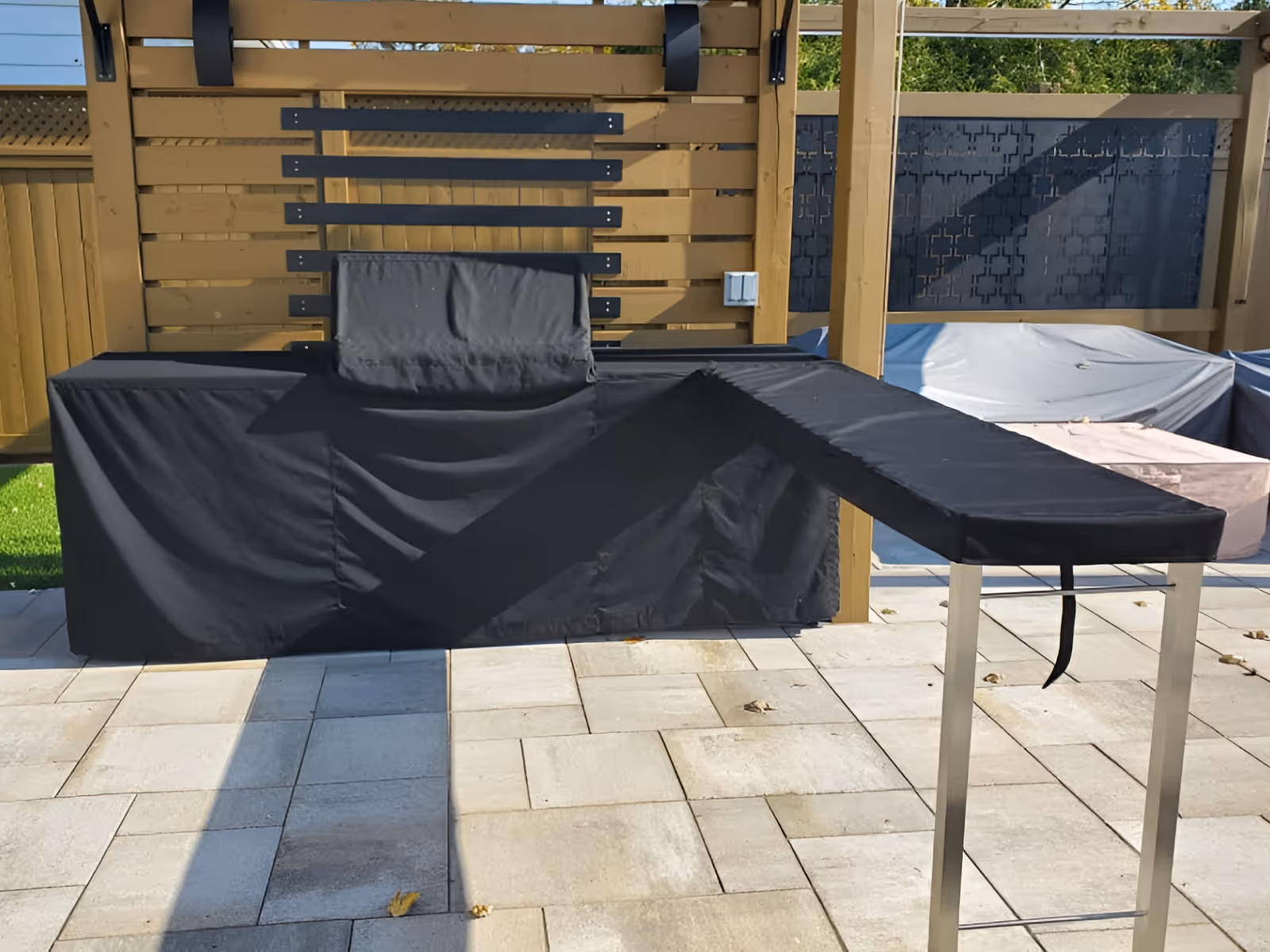 Outdoor grill with a custom black cover made of fabric, featuring a main body cover and a separate side table cover.