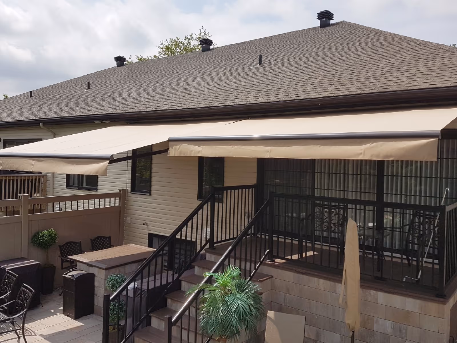 Outdoor patio area with black railings, beige retractable awnings attached to a house, and patio furniture.