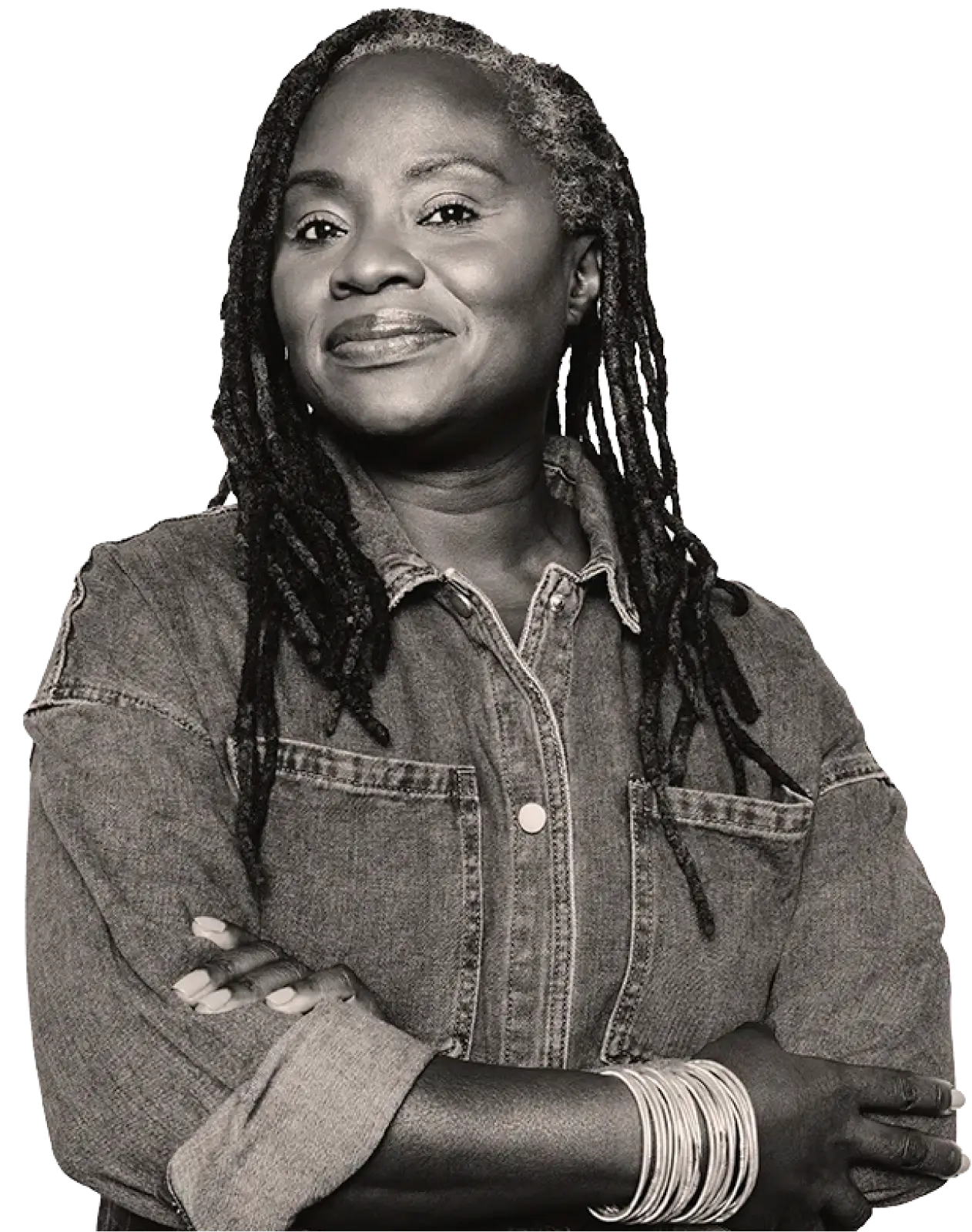 Confident woman with gray dreadlocks wearing a denim shirt and multiple bracelets, smiling with folded arms.
