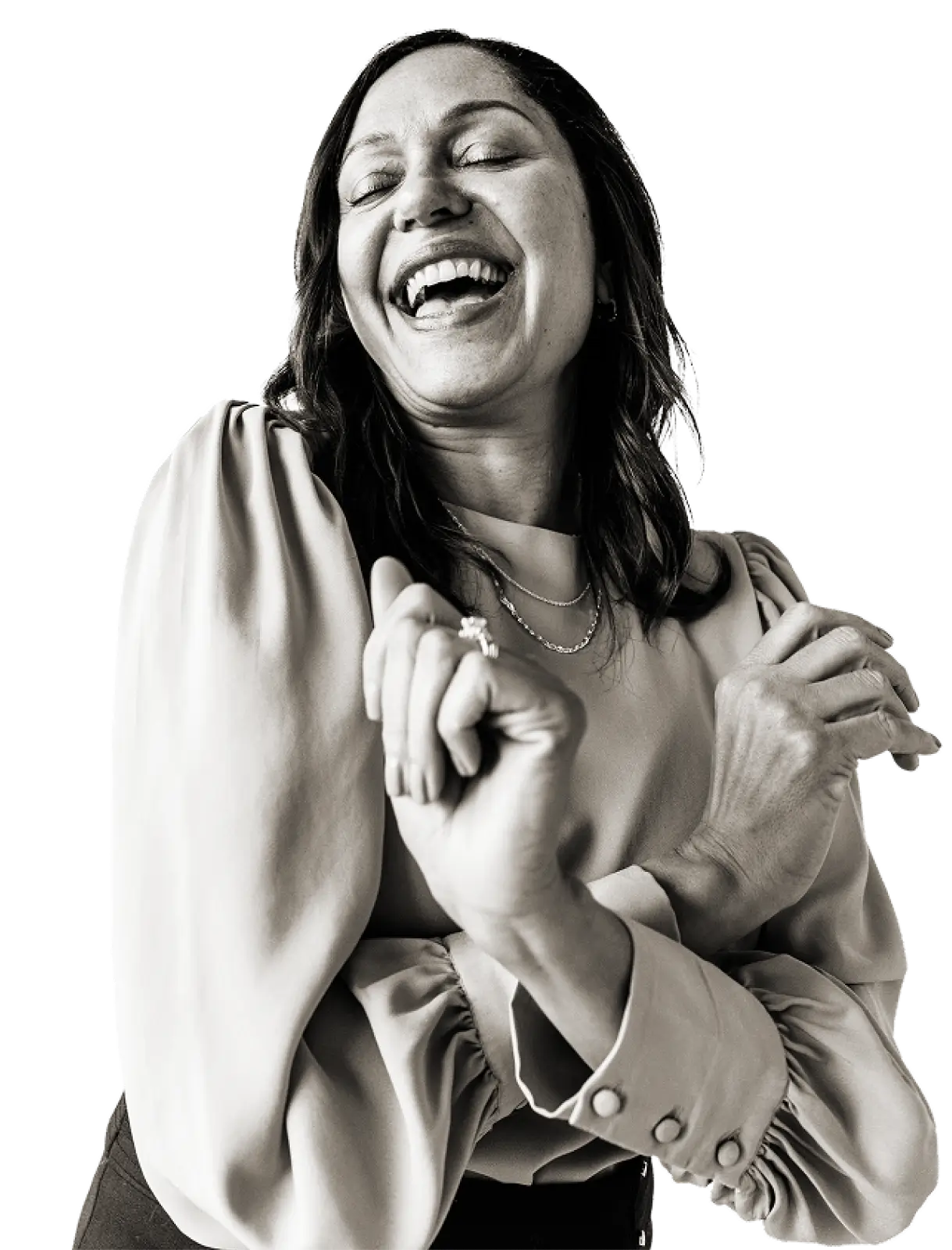 Woman with closed eyes smiling broadly and holding her arms crossed near her chest, wearing a long-sleeve blouse with buttons on the cuffs.