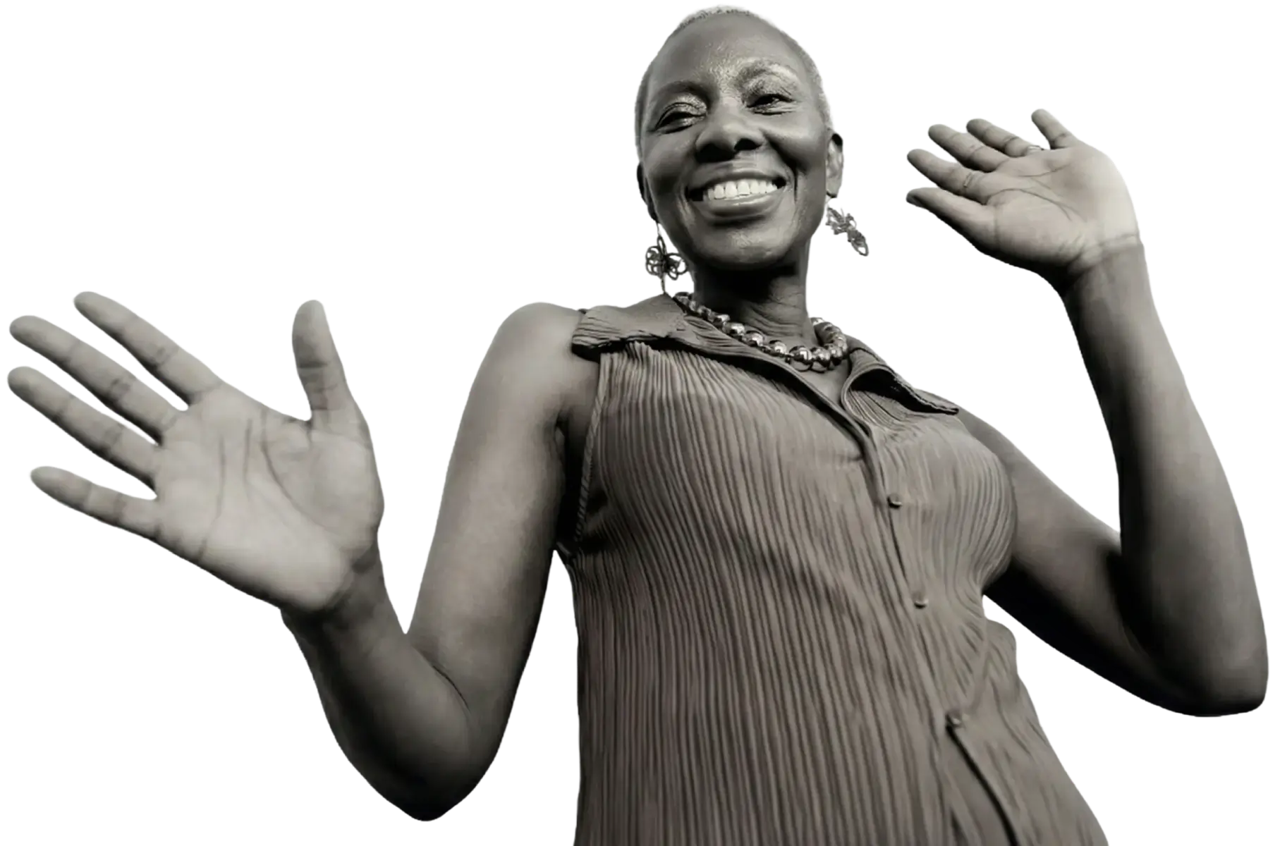 Smiling woman with short hair wearing a sleeveless pleated top and beaded necklace, raising both hands.