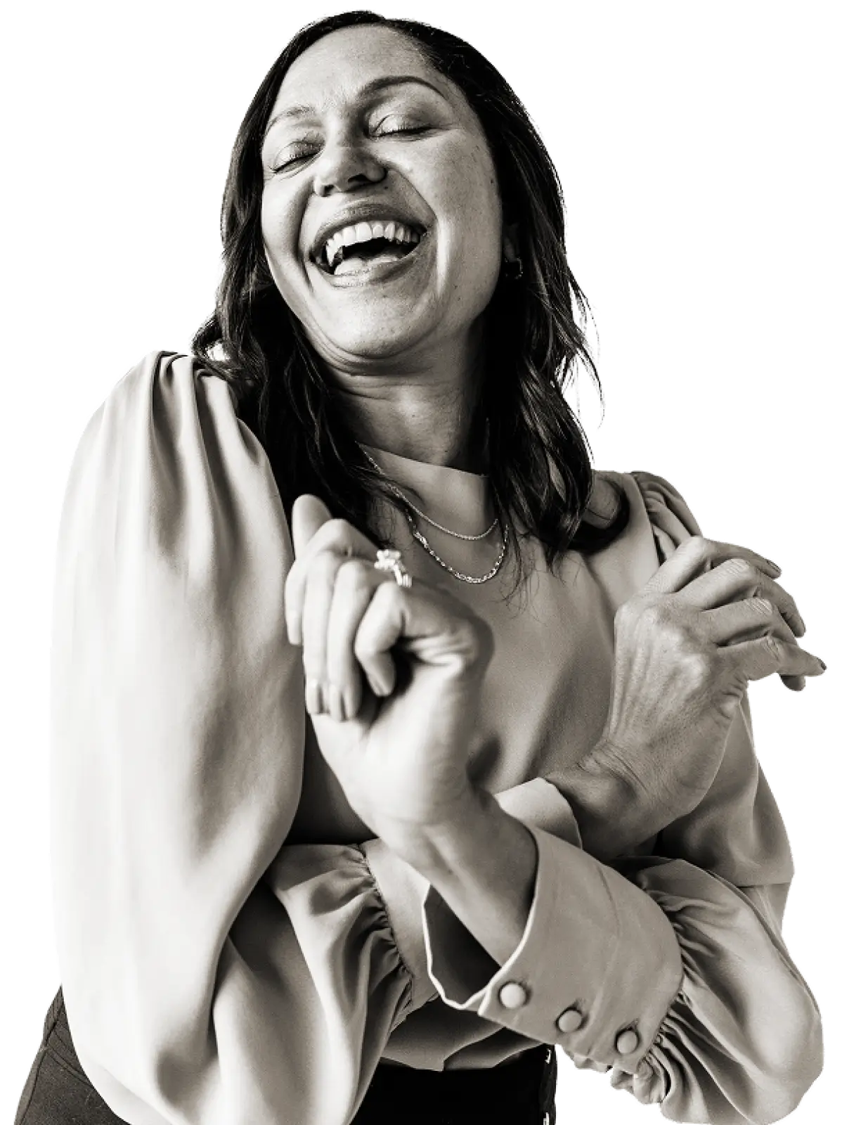 Smiling woman with closed eyes laughing, wearing a long-sleeve blouse and two necklaces.