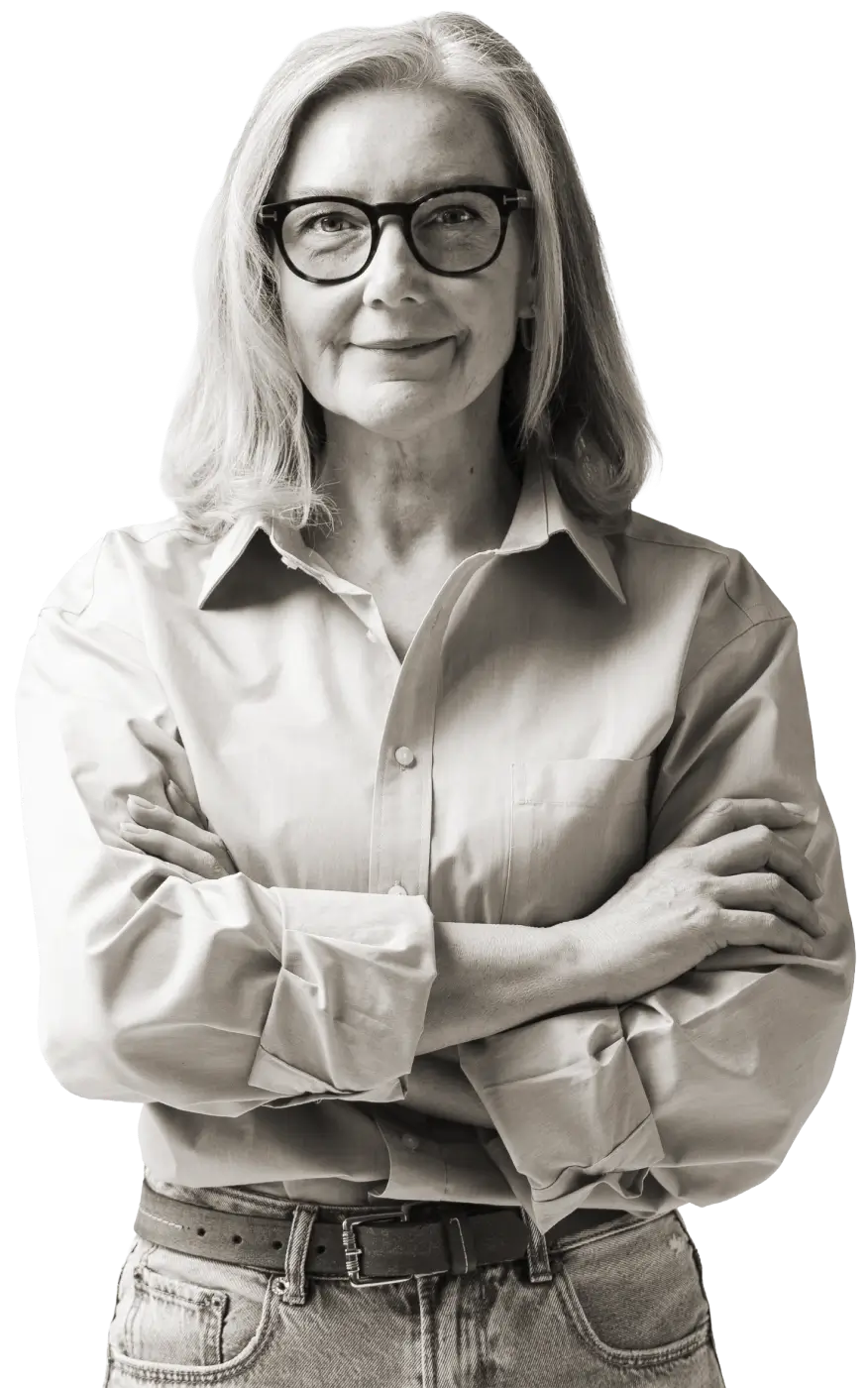 Confident older woman with glasses, arms crossed, wearing a light shirt and jeans.