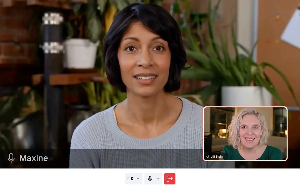 Smiling woman with short dark hair wearing a light gray sweater, seated indoors with plants and a corkboard in the background.