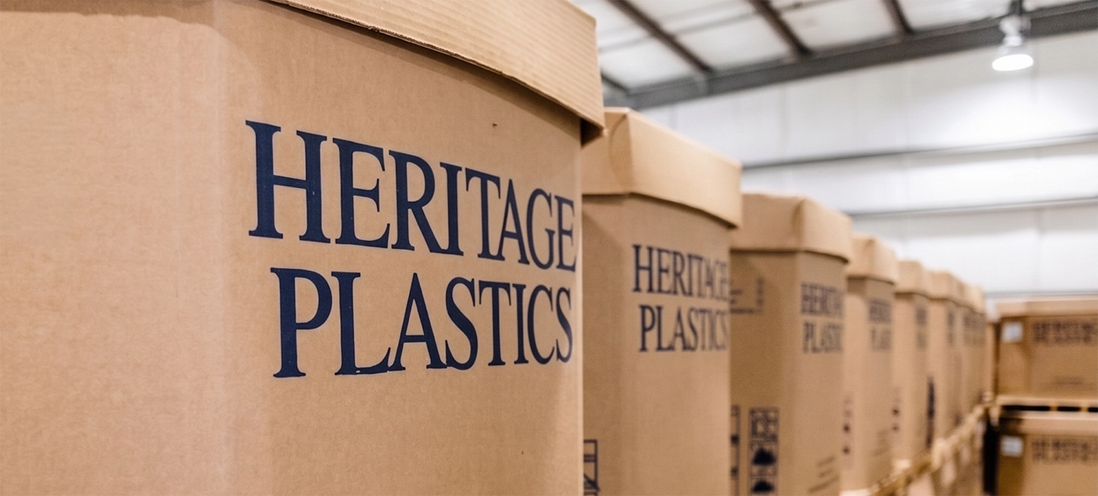 Row of large cardboard Heritage Plastics containers stacked indoors in a warehouse.