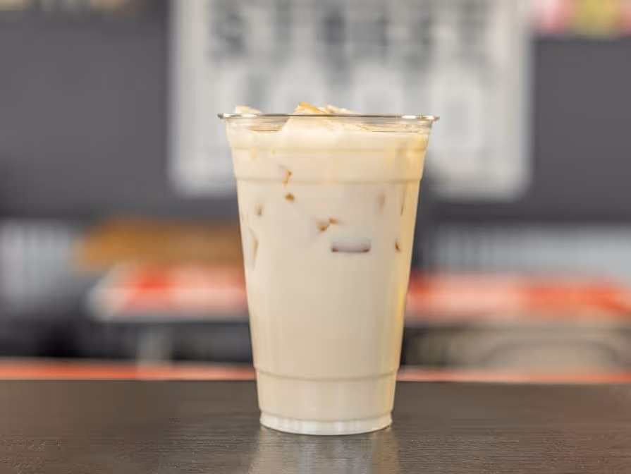 A clear plastic cup filled with agua de horchata placed on a dark table. The creamy beverage creates a refreshing and inviting tone, with a blurred cafe backdrop.