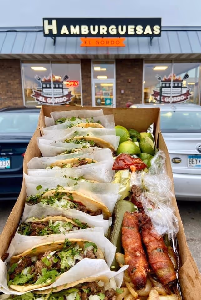 A box of food with a variety of items including tacos, limes, and meat.
