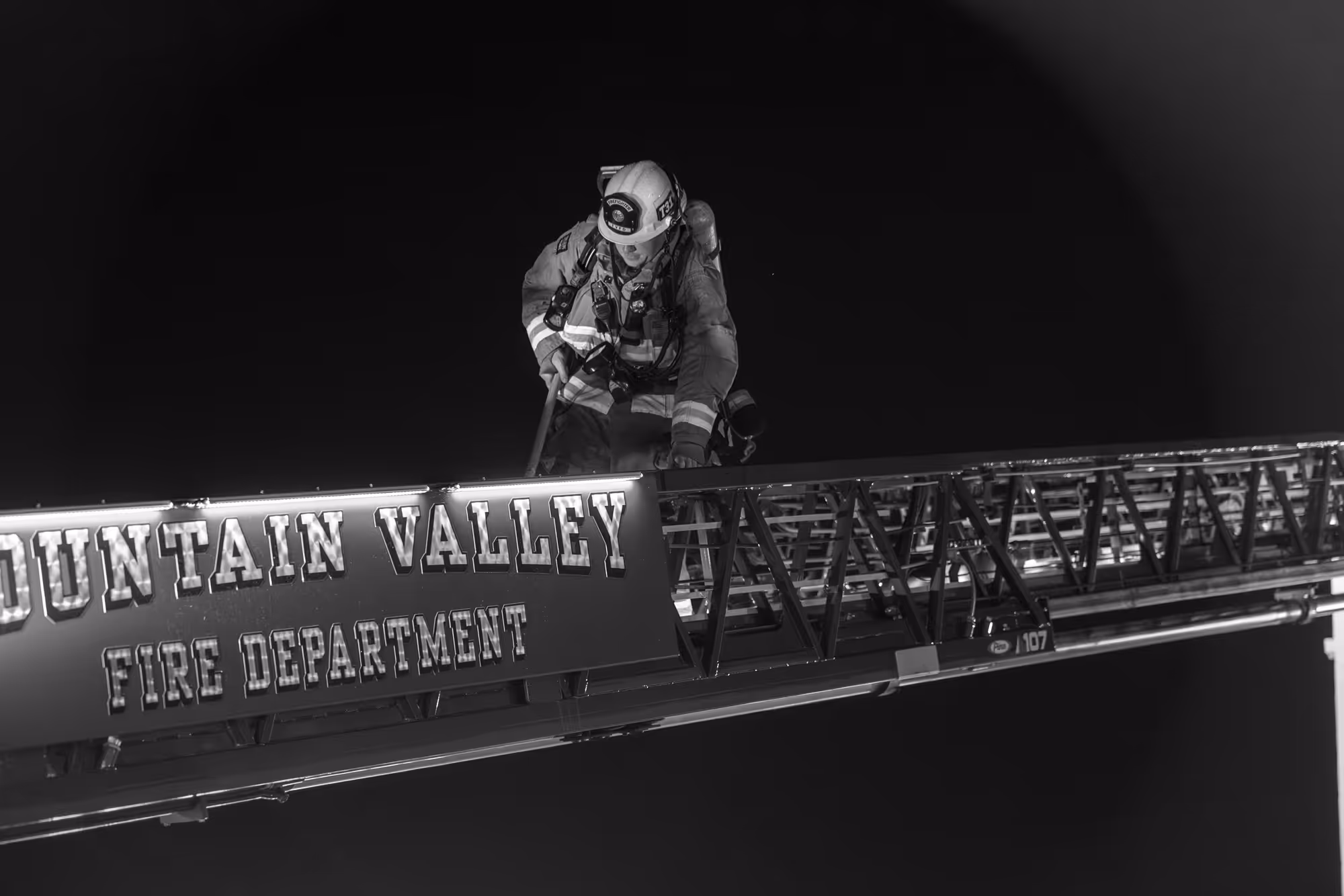 Aerial view of a long sandy beach with ocean waves on the left and a dense coastal town with buildings and streets on the right under a partly cloudy sky.