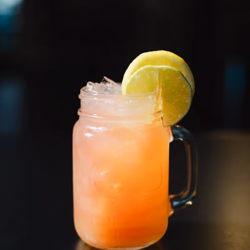 Iced orange-colored drink in a glass jar with slices of lemon and lime on the rim.