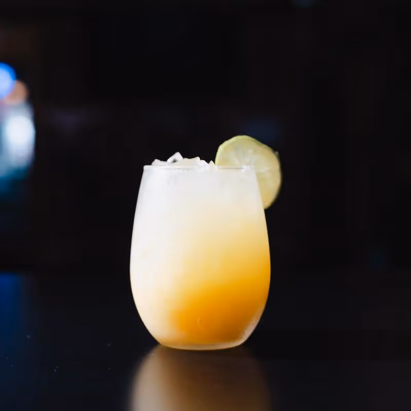 Chilled yellow-orange cocktail with crushed ice and a lime wheel garnish on a black reflective surface.