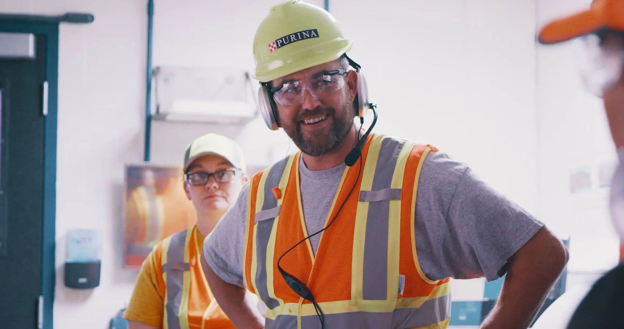Factory worker in orange jacket and white hard hat.