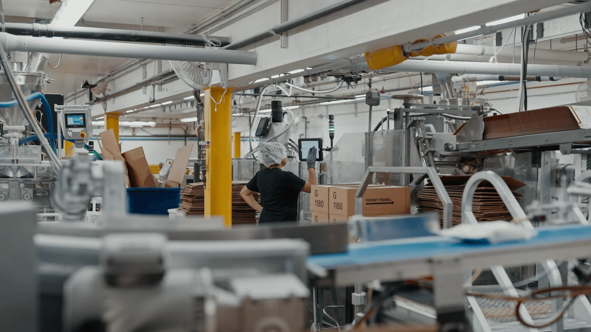 Factory worker wearing a hairnet walking through a production facility while reviewing information on a tablet.