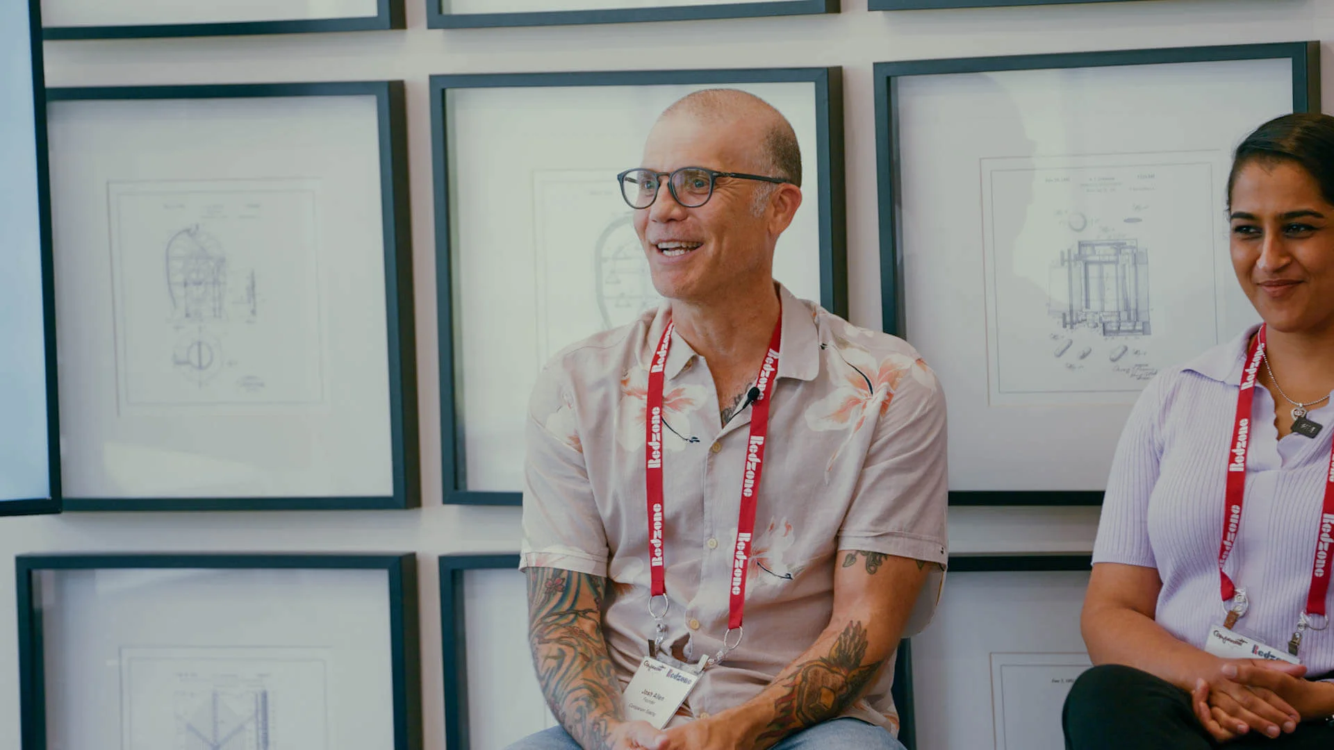 Two professionals wearing conference badges sitting and speaking during a filmed interview or testimonial.