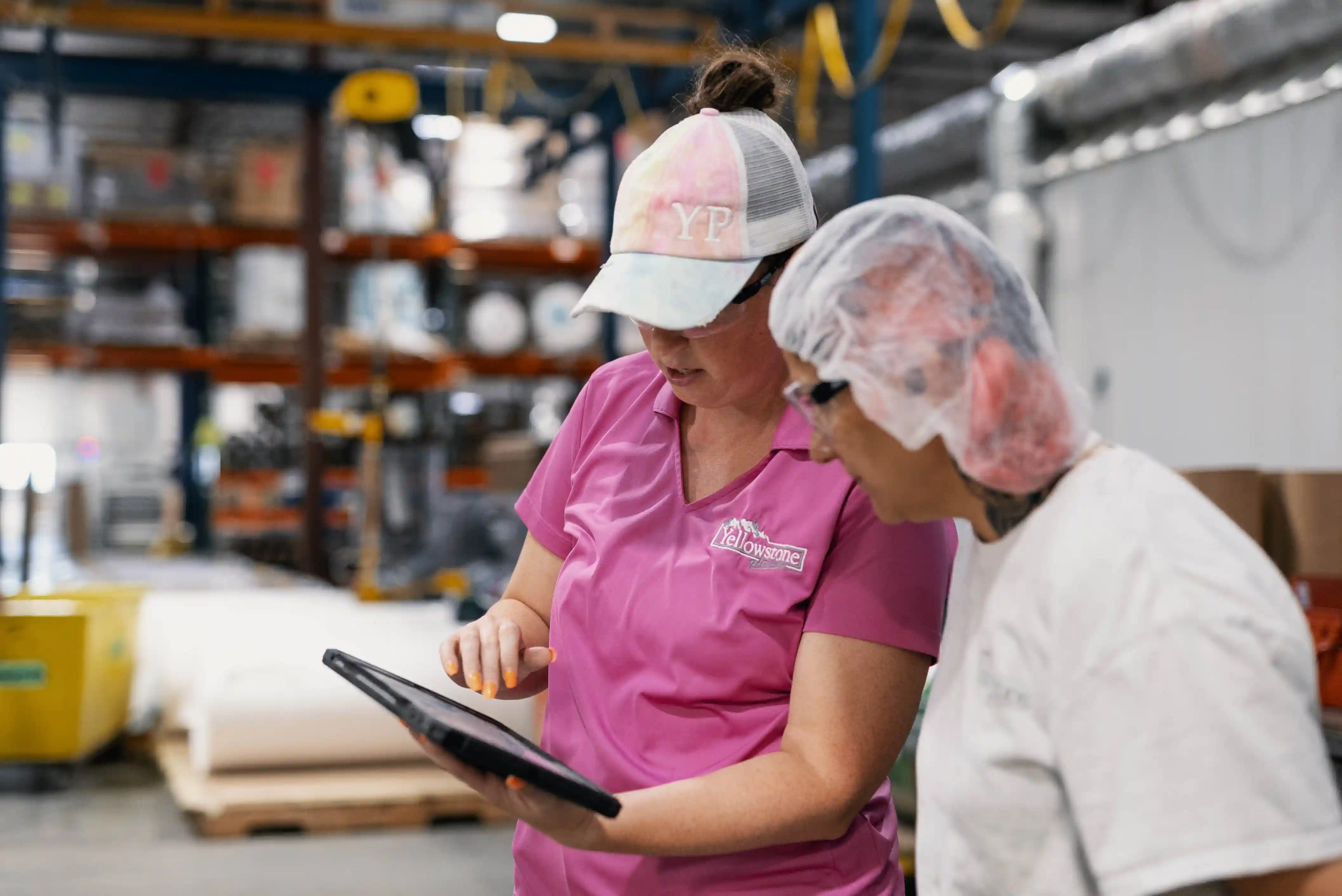 Des ouvriers d'usine portant des équipements de protection discutent des processus de production sur une tablette à l'intérieur d'une usine de transformation des aliments.