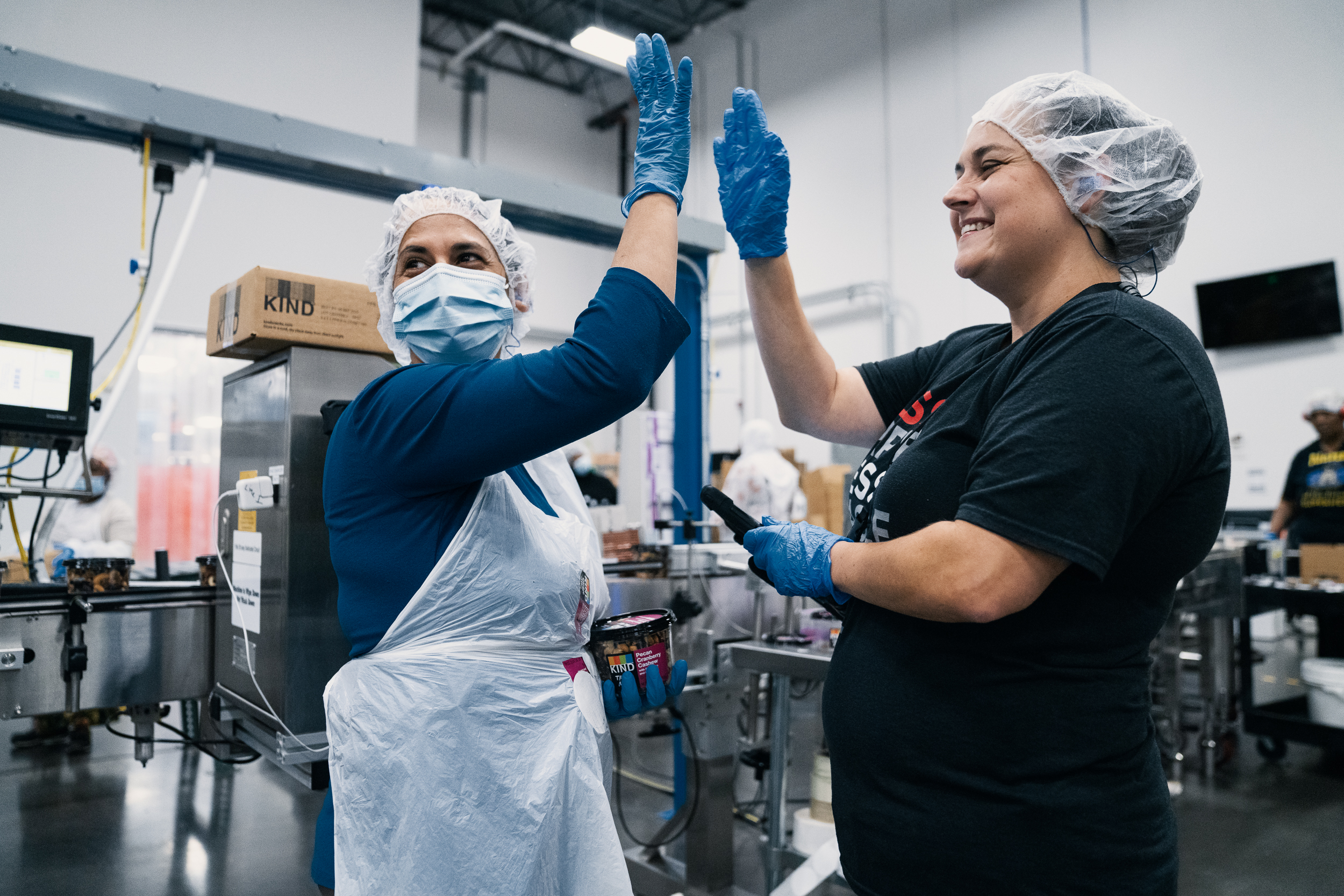 Two women high fiving on a factory floor wearing hairnets.