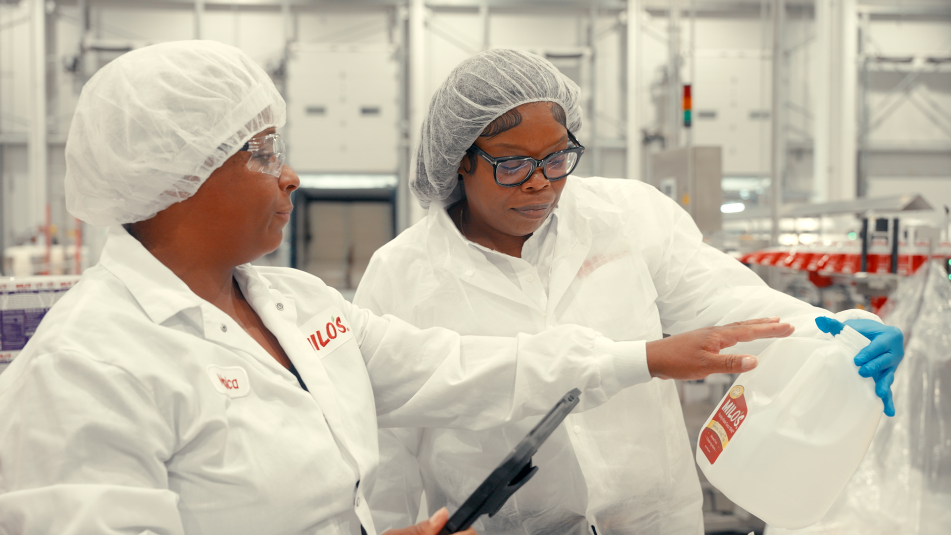 Factory workers wearing hairnets reviews information on a tablet in an plant setting.