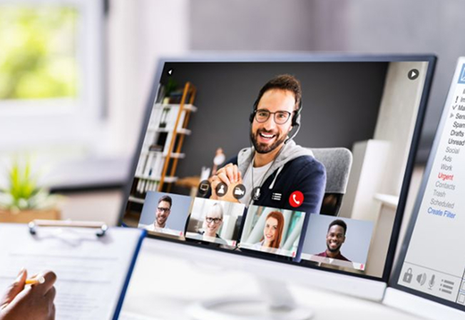 Computer screen showing a video conference with five participants, one man with glasses and headset smiling prominently in the main window.