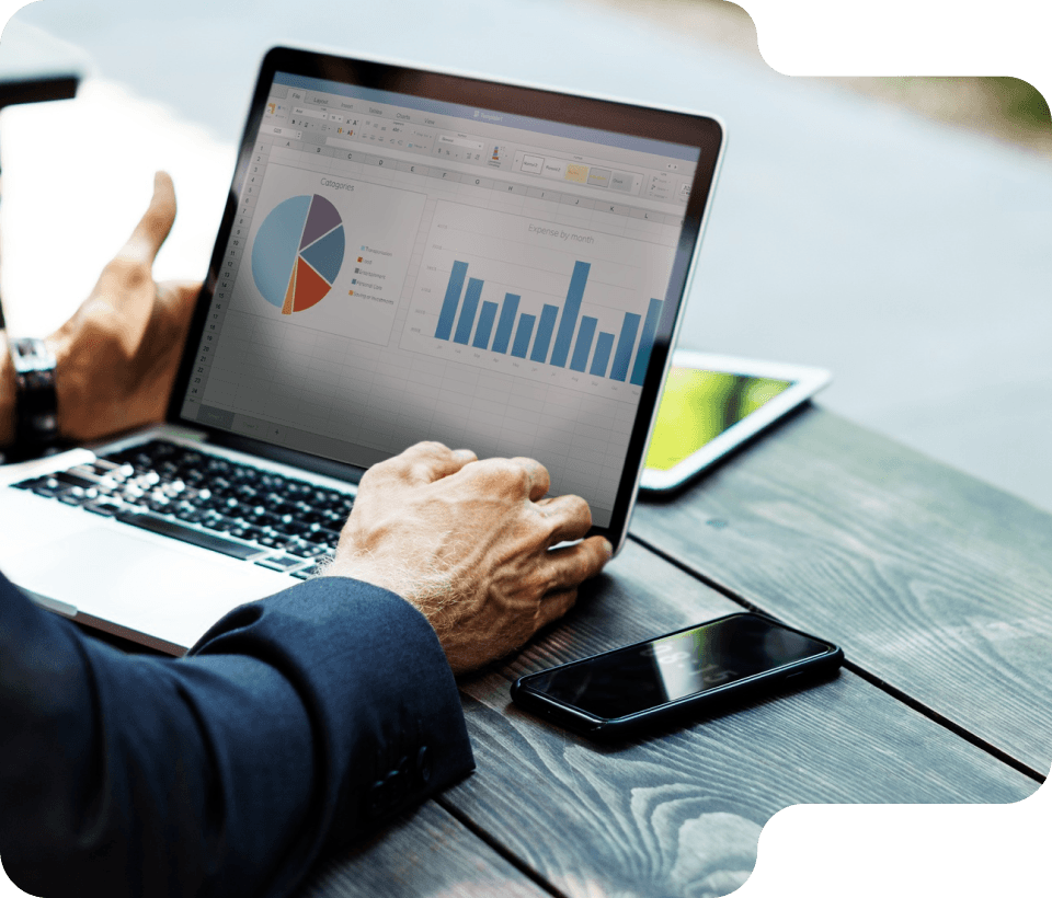 Person analyzing charts and graphs on a laptop, with smartphone and tablet on a wooden table.